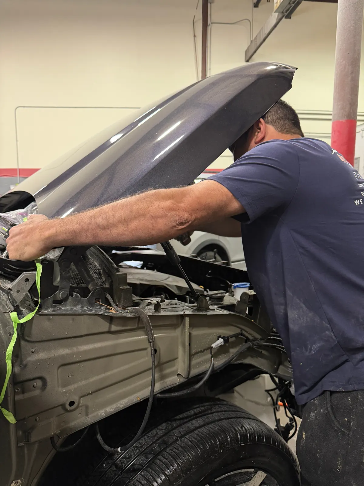 Technician lifting a hood to inspect hidden damage behind the bumper
