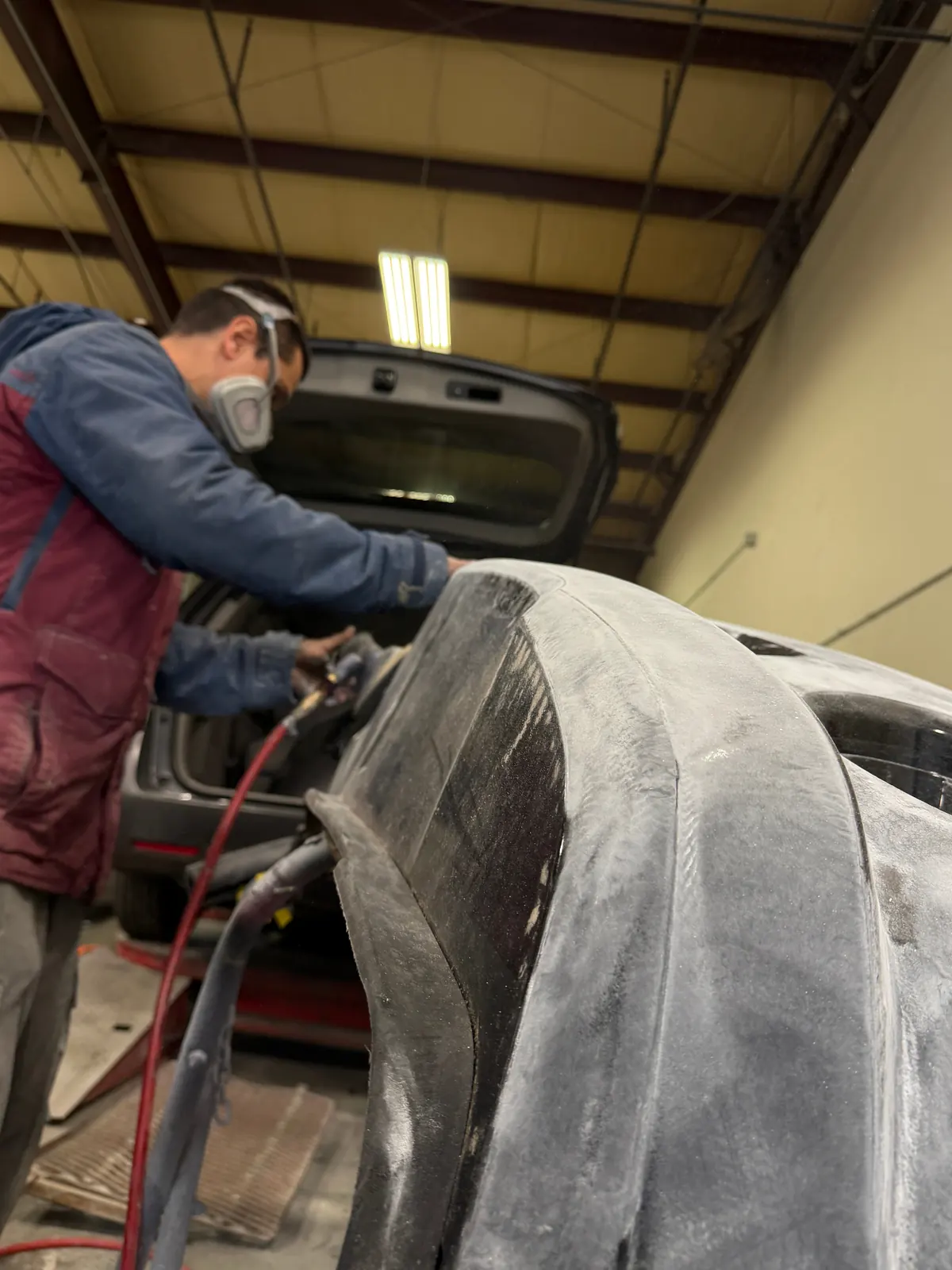 Technician sanding body filler to level a repaired panel before primer
